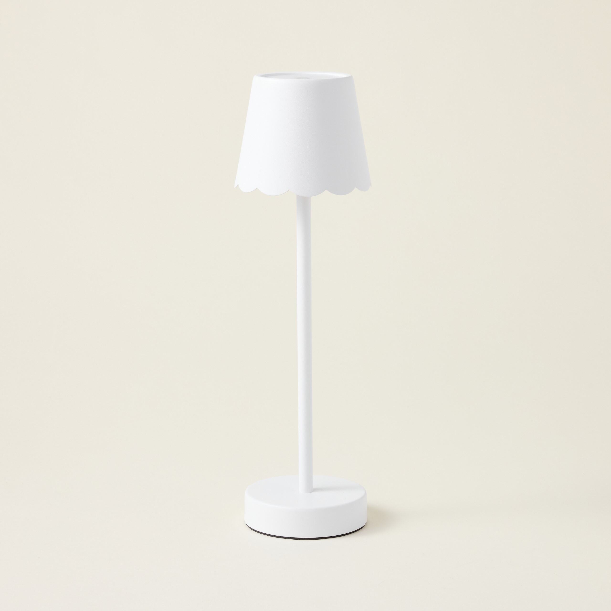 A white iron cordless table lamp with a scalloped edge shade.