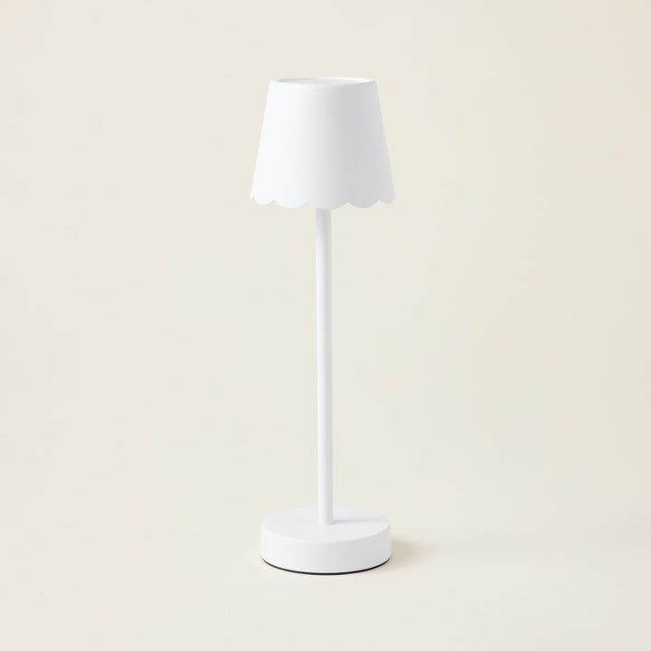 A white iron cordless table lamp with a scalloped edge shade.
