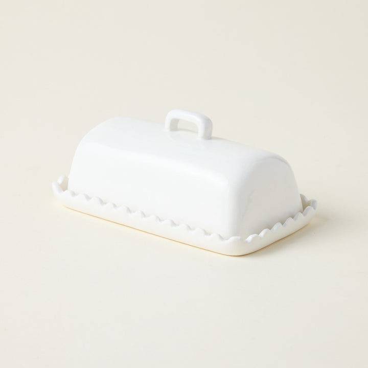 A white butter dish with a scalloped design and a reactive glaze finish.
