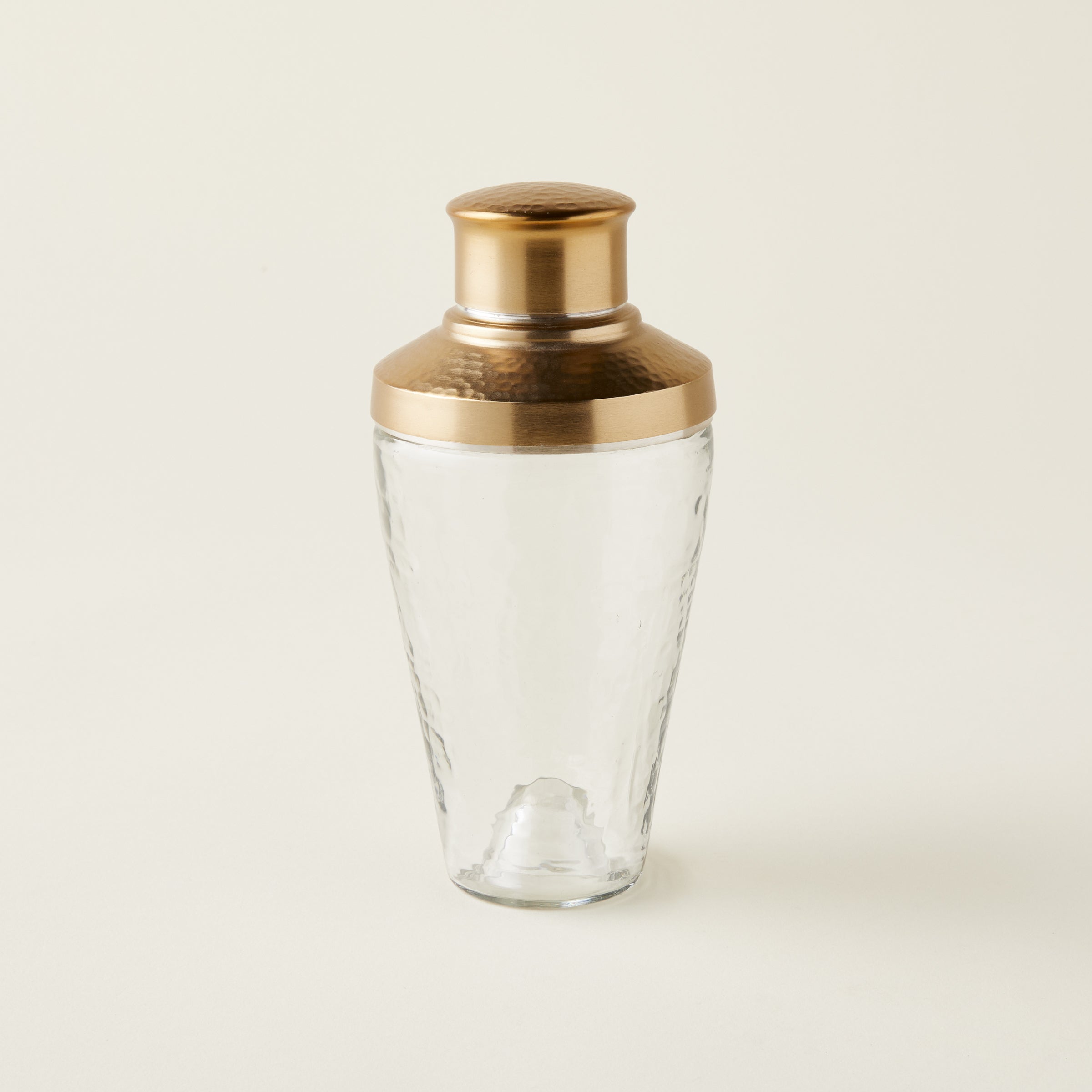 Glass cocktail shaker with a rippled texture and a brass lid.