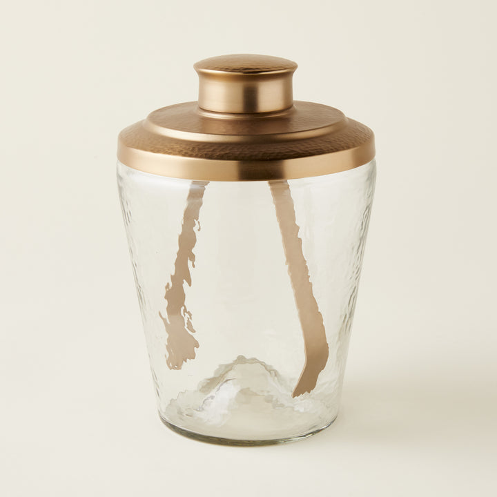 Ana glass ice bucket with a pebbled texture and a hammered brass lid, accompanied by brass tongs.