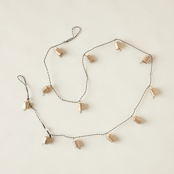 A garland of small antique gold bells strung on a black and white rope.