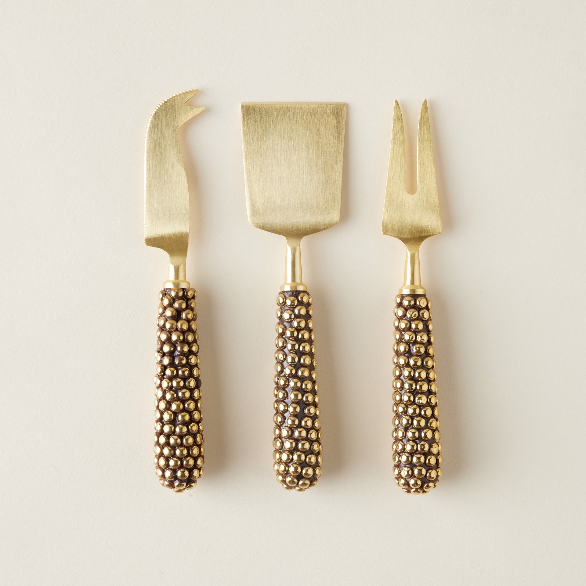 A set of three decorative cheese knives with cast brass handles featuring a beaded texture.