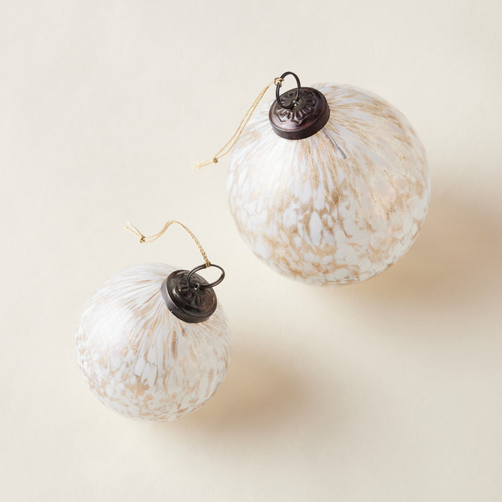 A set of two clear glass ball ornaments in two sizes, with shimmering gold and white confetti inside.