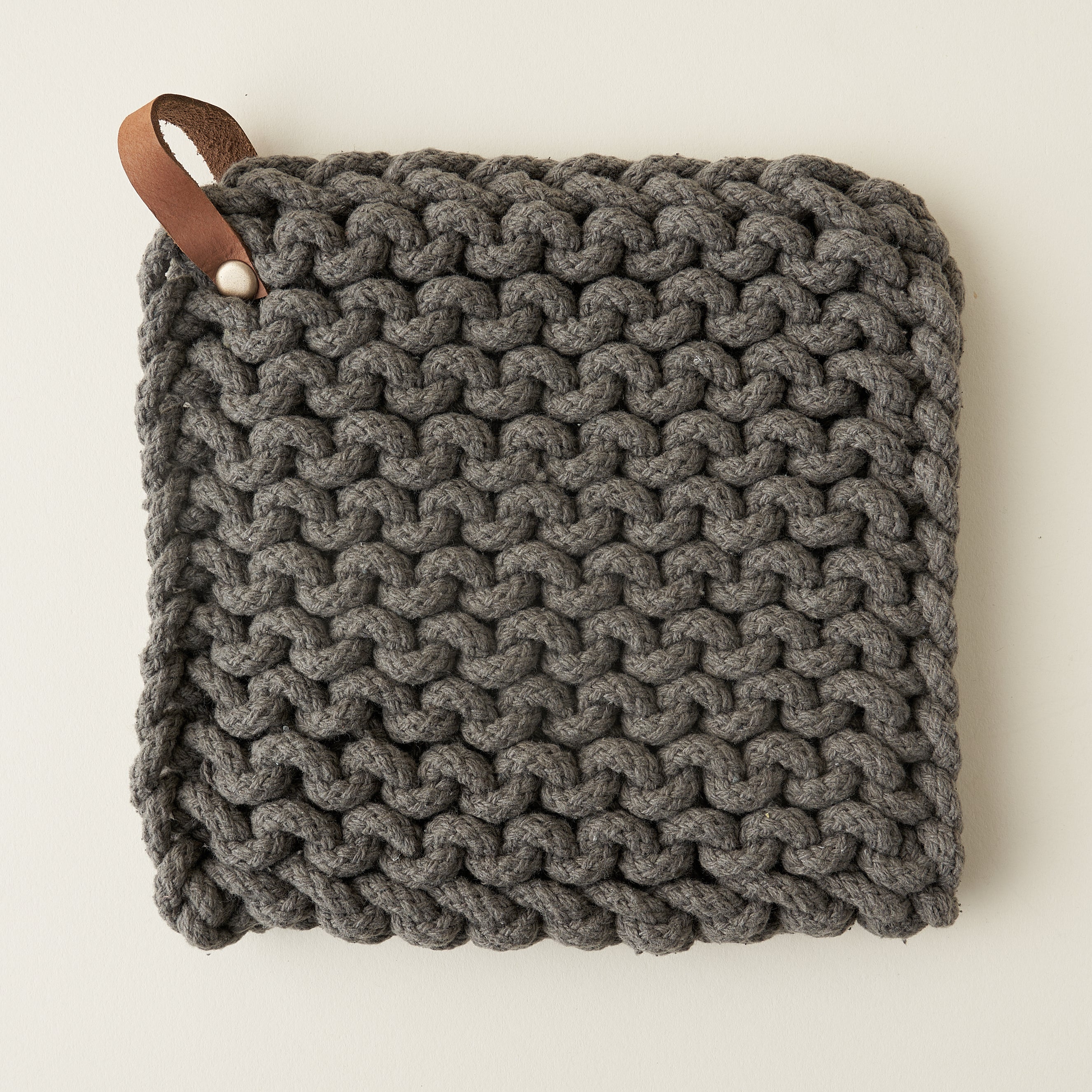 A square, crocheted pot holder made of soft cotton with a leather loop for hanging.