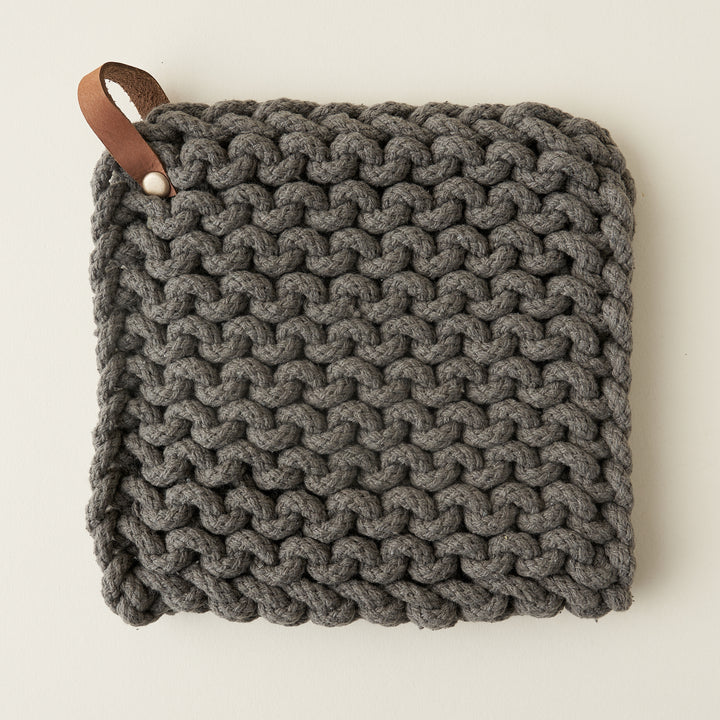 A square, crocheted pot holder made of soft cotton with a leather loop for hanging.