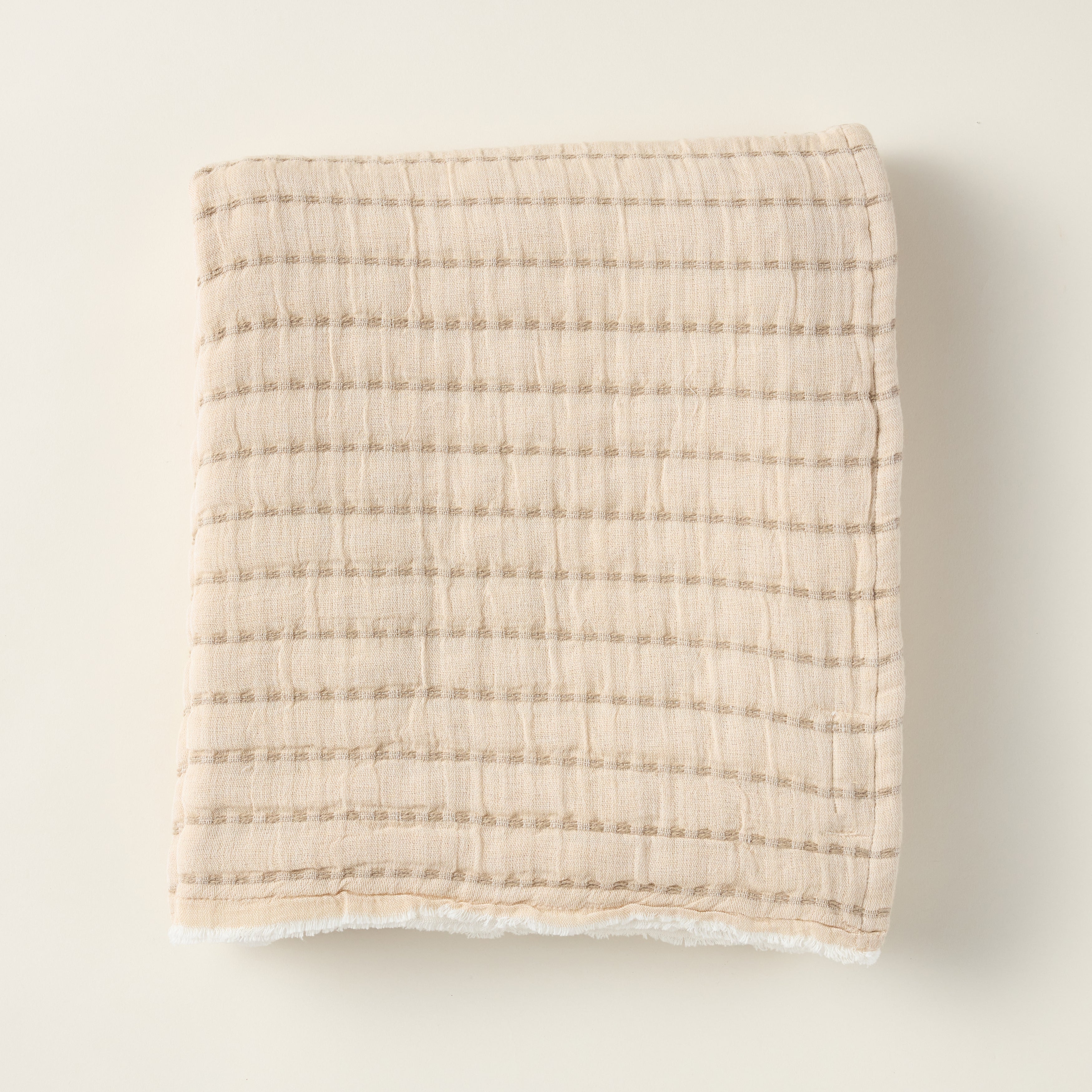 Two-tone double gauze cotton throw blanket on a sofa, with a neutral and brown side.