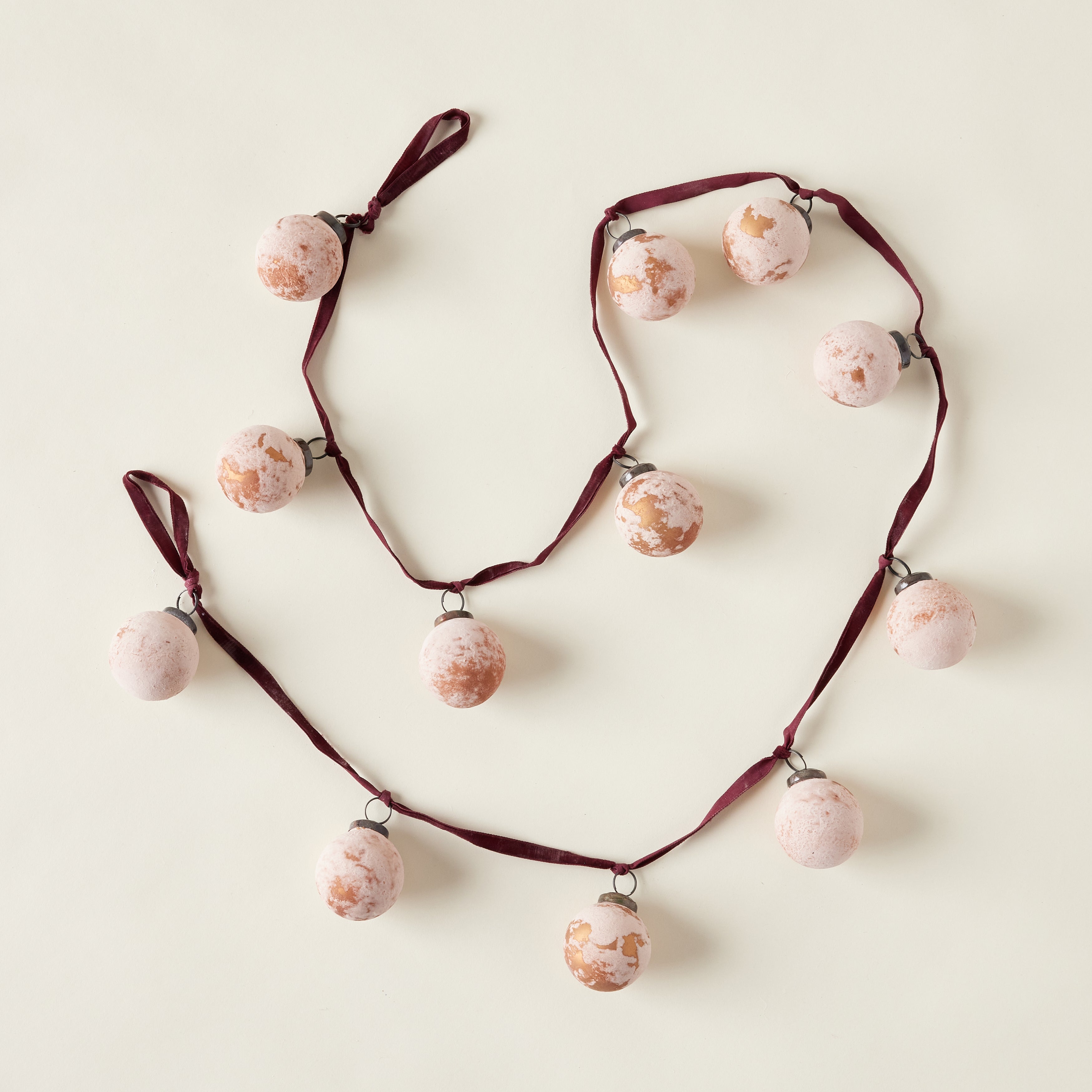 A garland made of frosted, distressed glass ball ornaments in a deep berry color, strung together with a burgundy velvet ribbon.