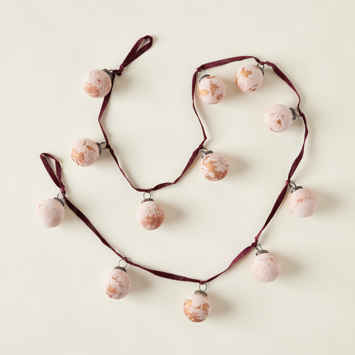 A garland made of frosted, distressed glass ball ornaments in a deep berry color, strung together with a burgundy velvet ribbon.