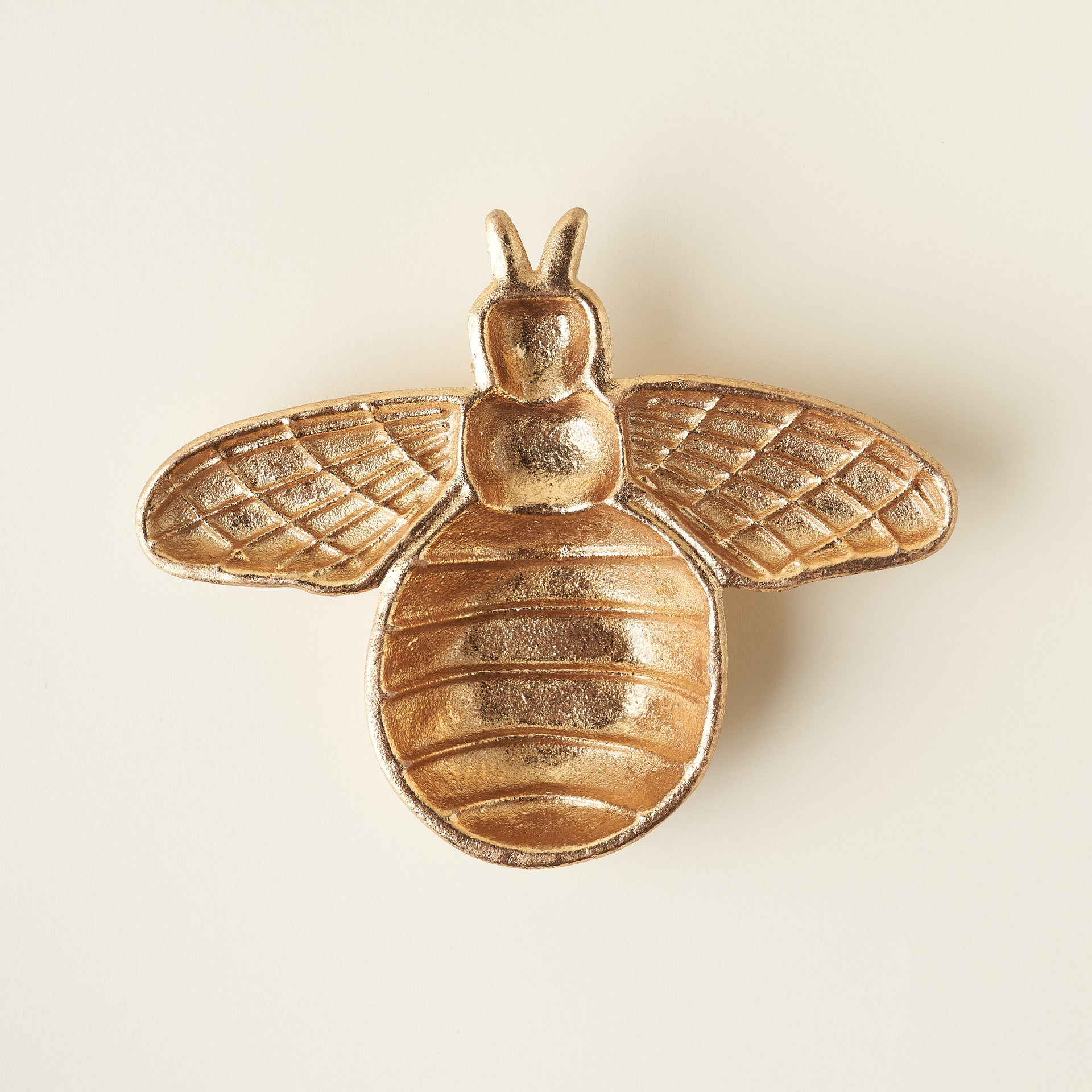 A small, decorative dish with a detailed raised bee design in the center and a rich gold finish.