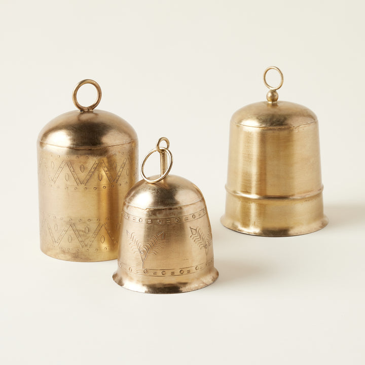 A collection of three decorative antique brass bells in small, medium, and large sizes, all with an etched metal finish.