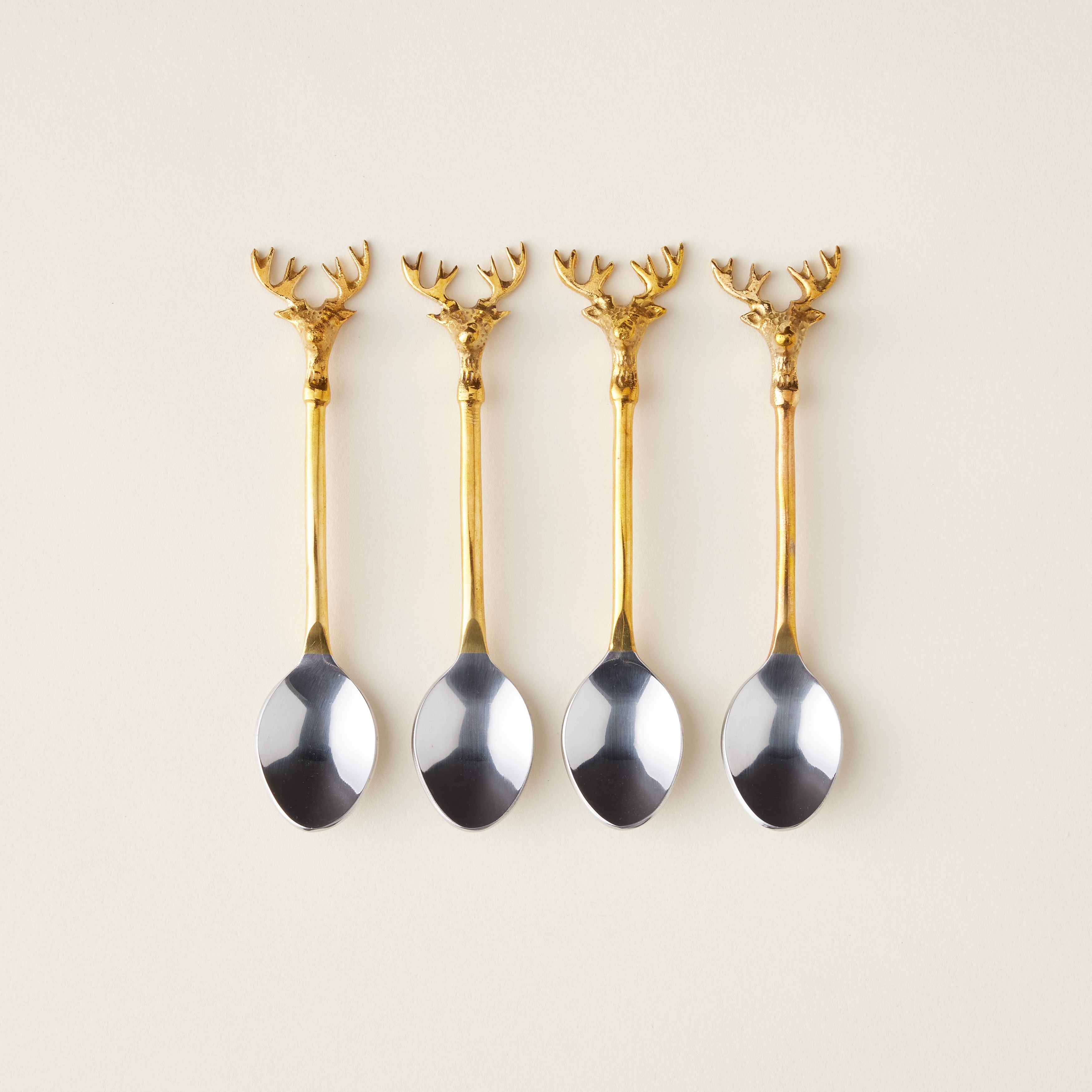 A set of four stainless steel spoons with gold-finished handles and a reindeer design.