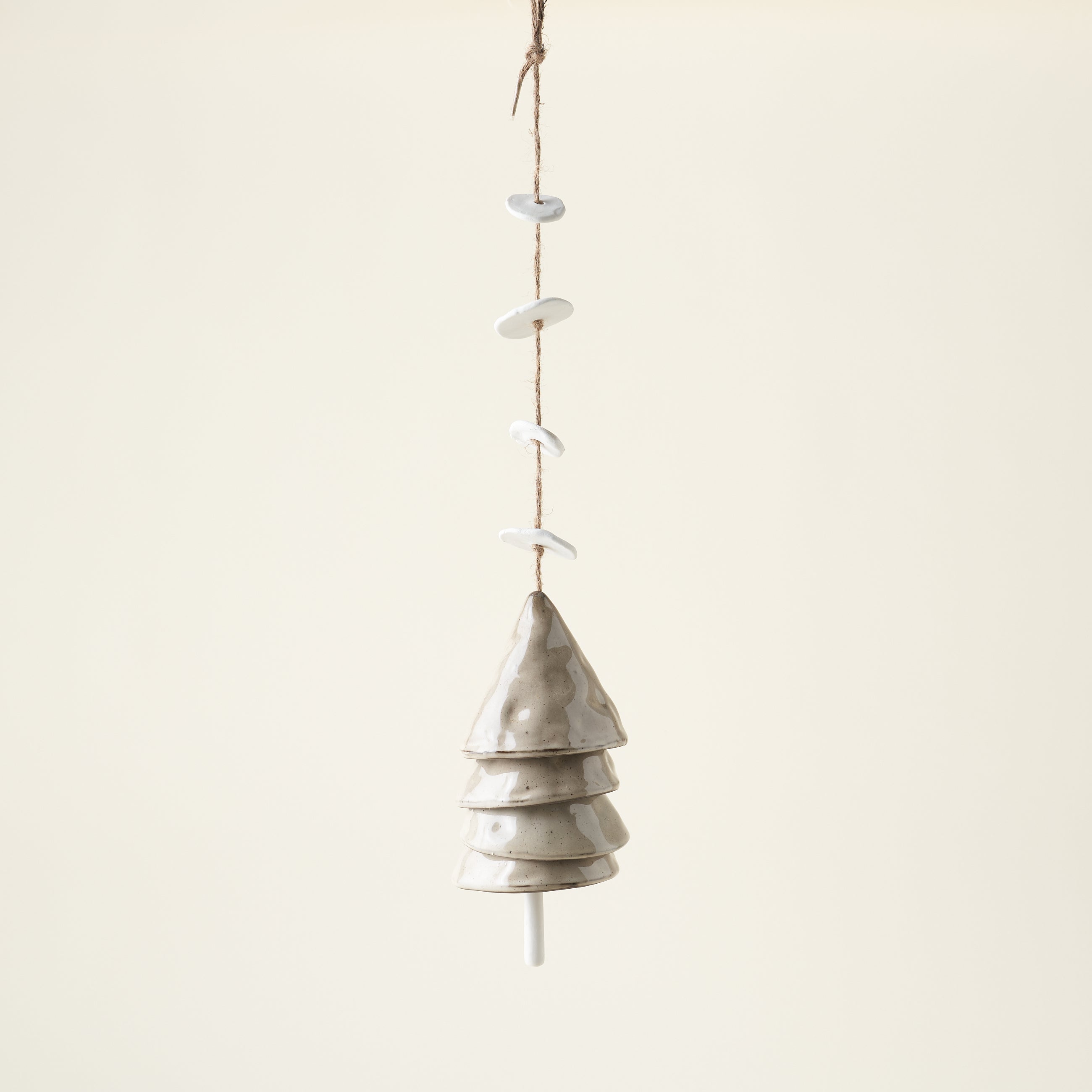 A set of hanging stoneware bells in beige and white with a jute string.