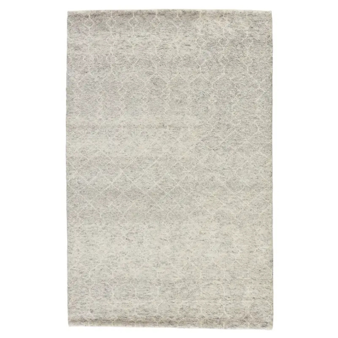 A hand-knotted Indira rug with a gray backdrop, a white diamond trellis design, and a scalloped edge.