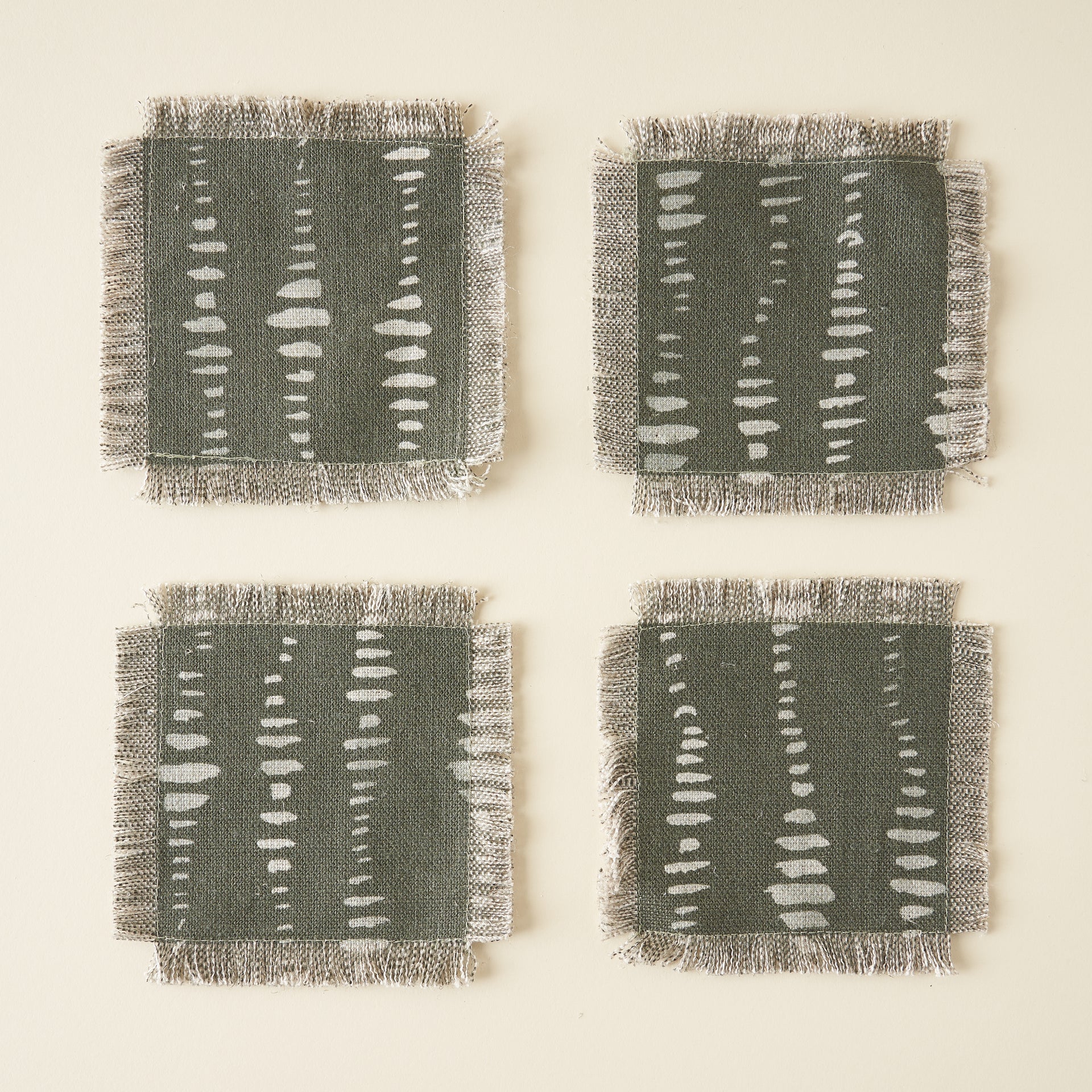 A set of four square textile coasters with a unique pattern and decorative fringe edges.