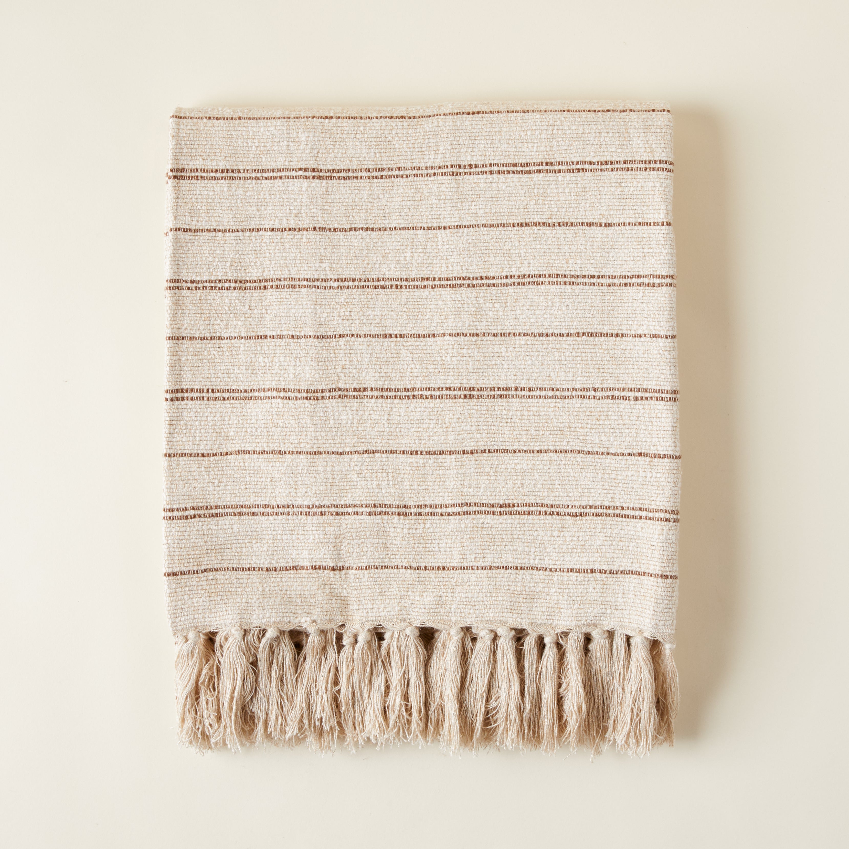 Hand-woven Kenna blanket with a ribbed texture and warm chestnut stripes on a neutral background.
