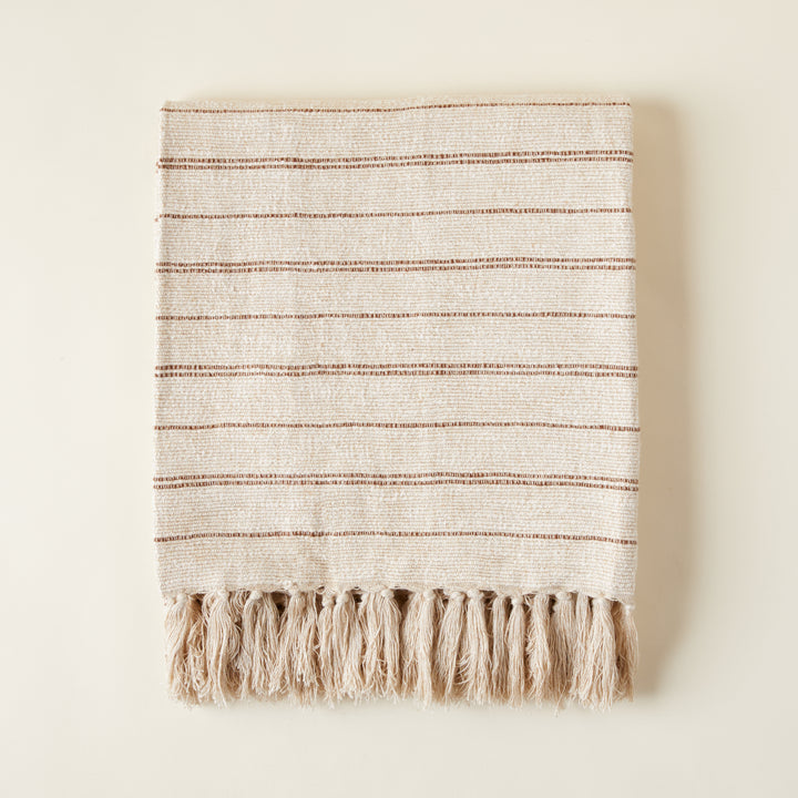 Hand-woven Kenna blanket with a ribbed texture and warm chestnut stripes on a neutral background.