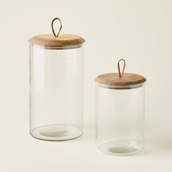 Set of two glass canisters with mango wood lids and leather pulls, shown in different sizes.