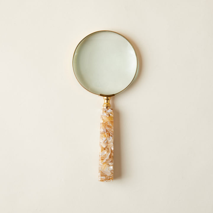 A decorative magnifying glass with a sleek brass frame and a handle made of iridescent mother-of-pearl.