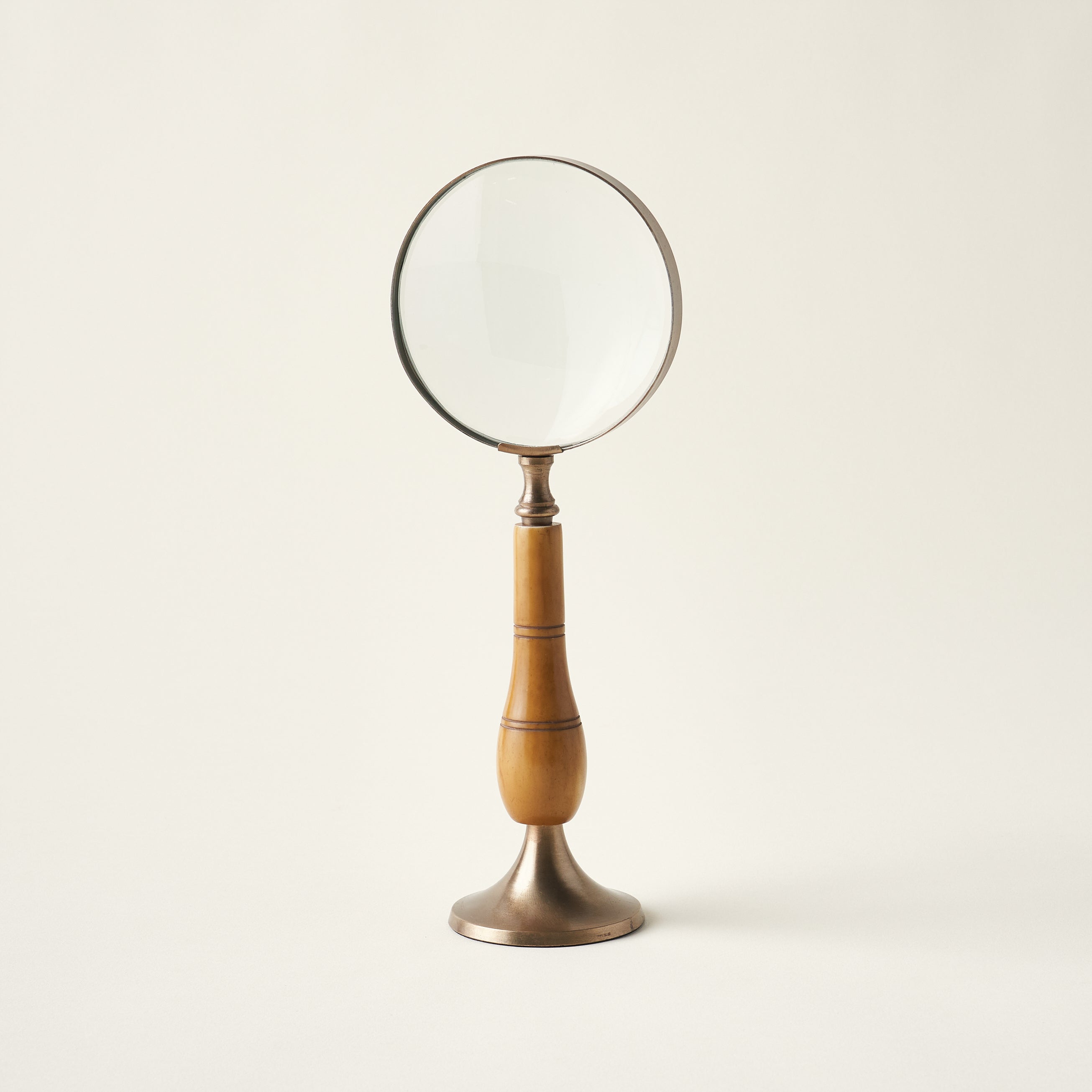 Antique magnifying glass on a stand with a brass and bone body and a timeless, heirloom design.