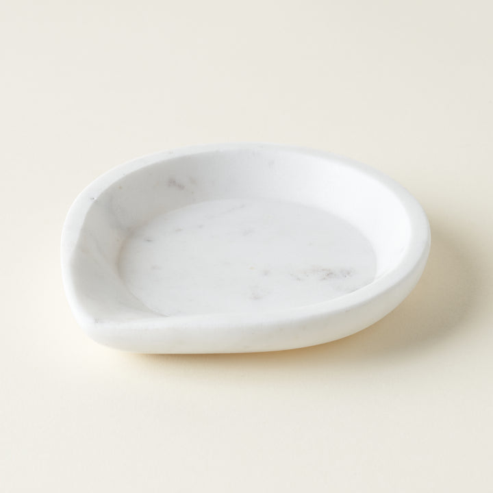 A smooth, white marble spoon rest with a carved indentation for holding utensils.