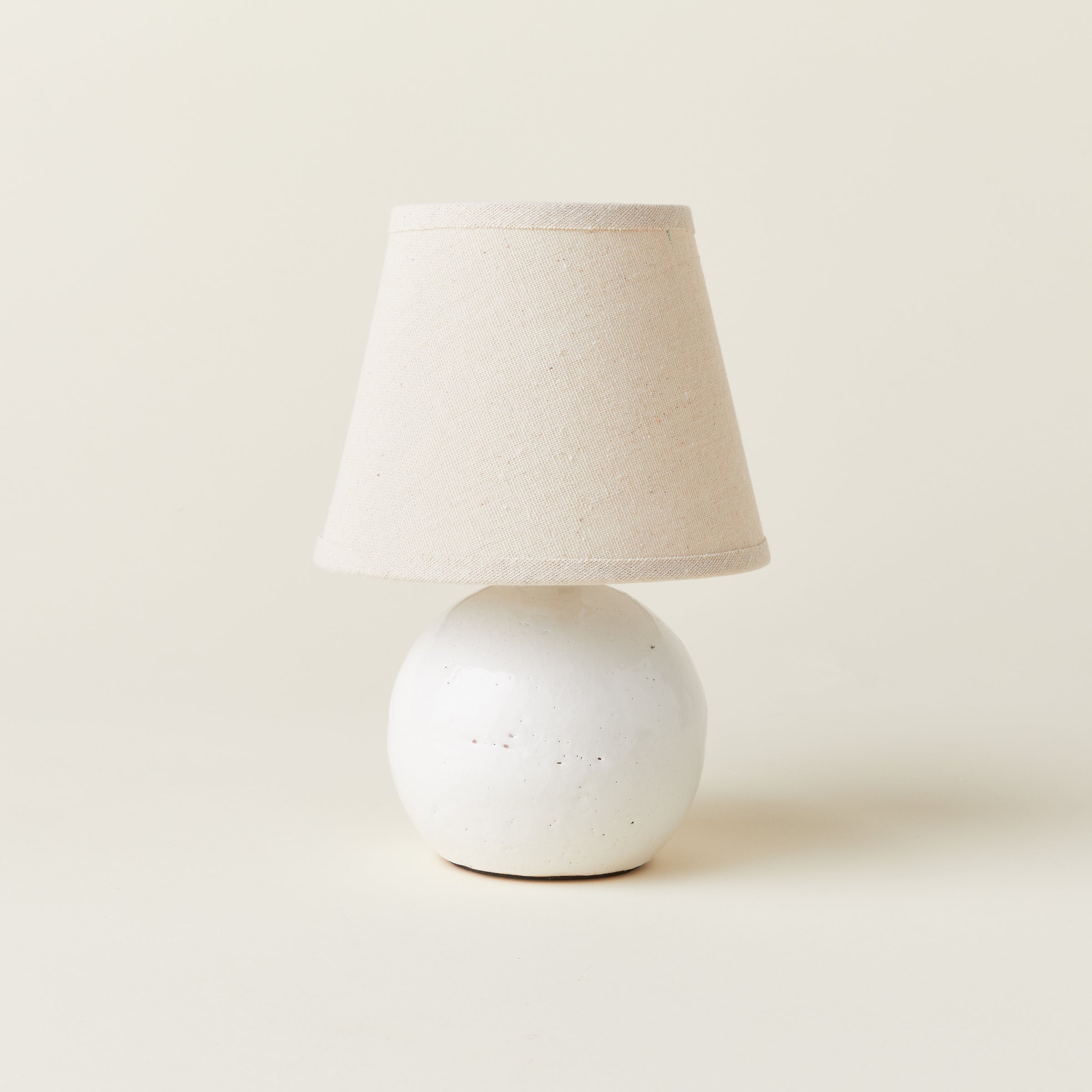 A petite off-white ceramic lamp with a textured cream-colored shade.
