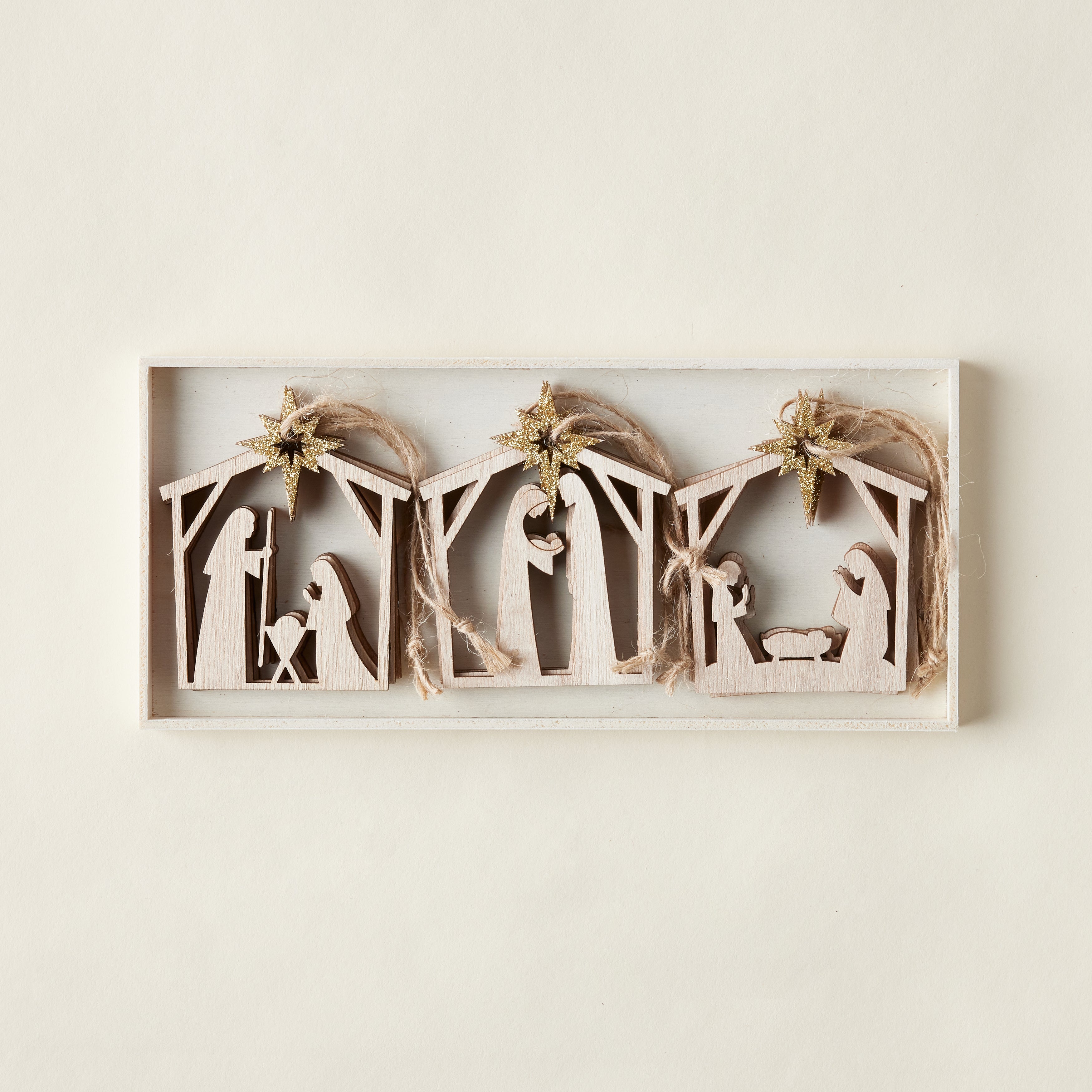 A set of nine laser-cut wooden ornaments, each depicting a different nativity scene with a gold glitter star.