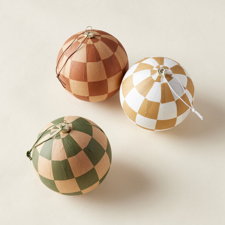 A collection of three hand-painted, lightweight paper mache ornaments, each with a unique checkerboard pattern in black, red, and sage green, styled together.