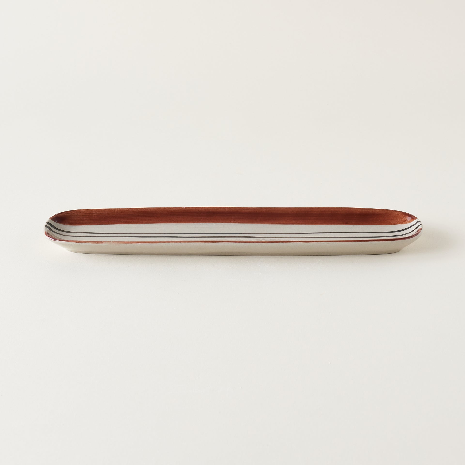 Oval stoneware tray with a hand-painted black and deep orange striped design.