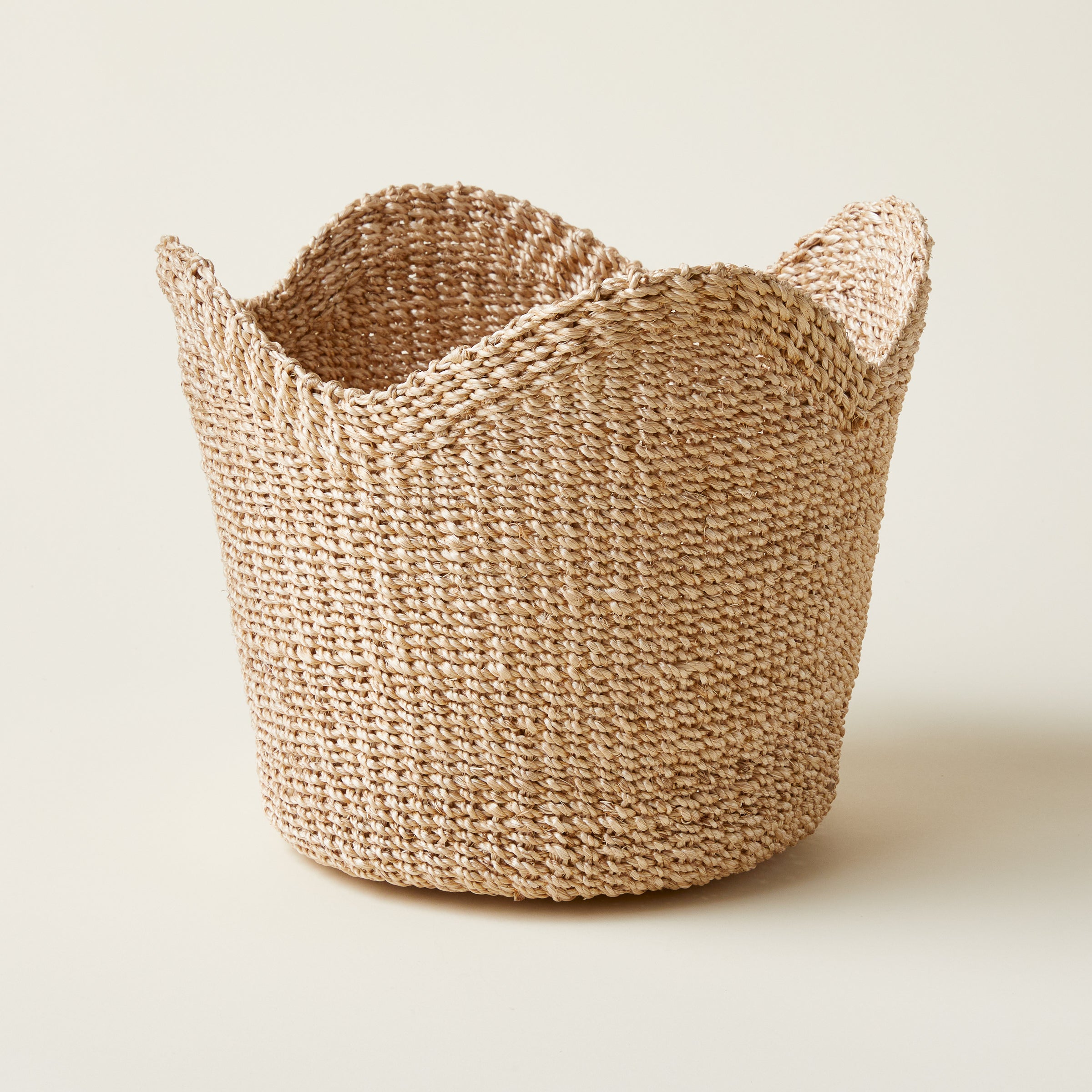 A hand-scalloped, natural-toned basket made from woven manila hemp.
