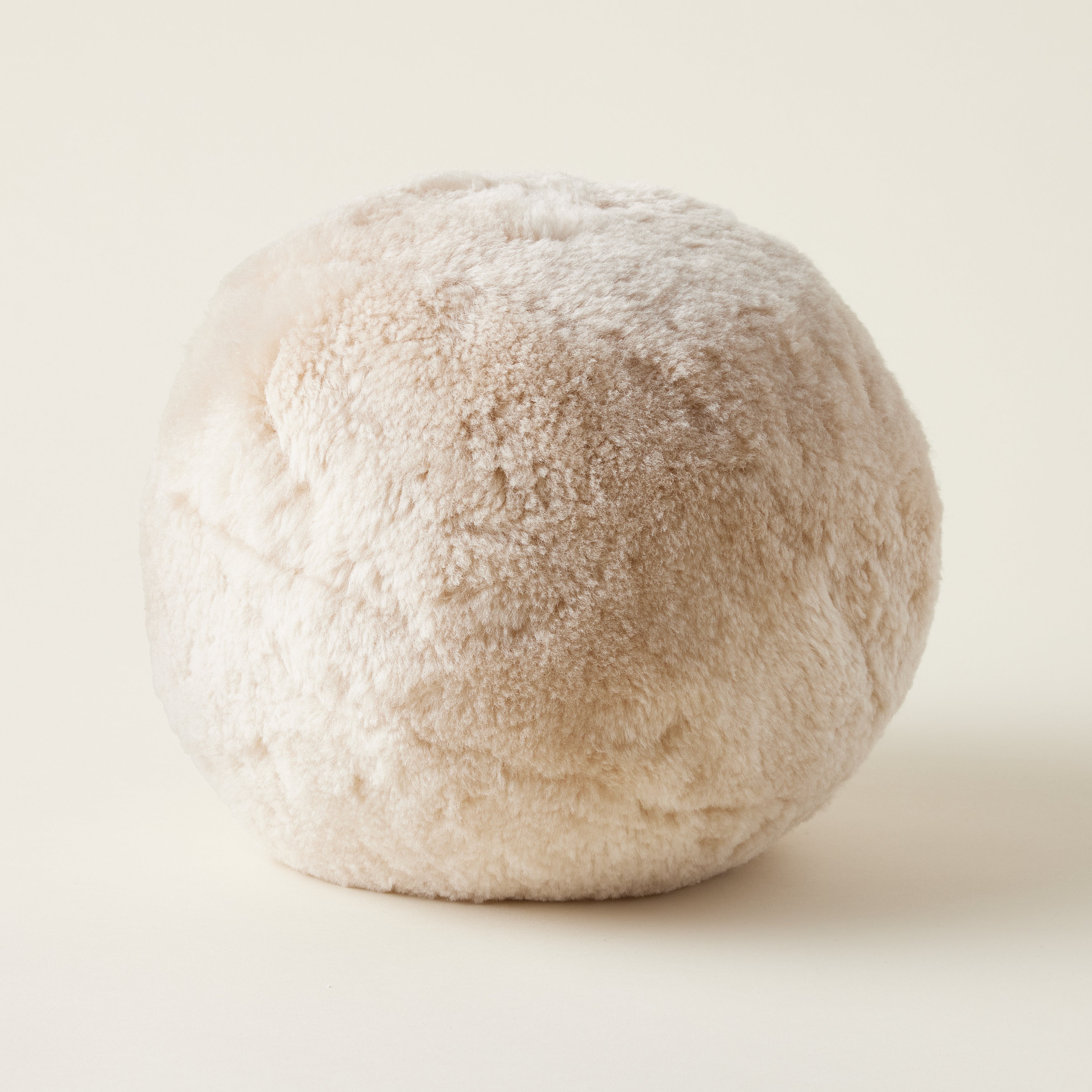 Sheepskin orb pillow, round and plush with a soft, natural texture.