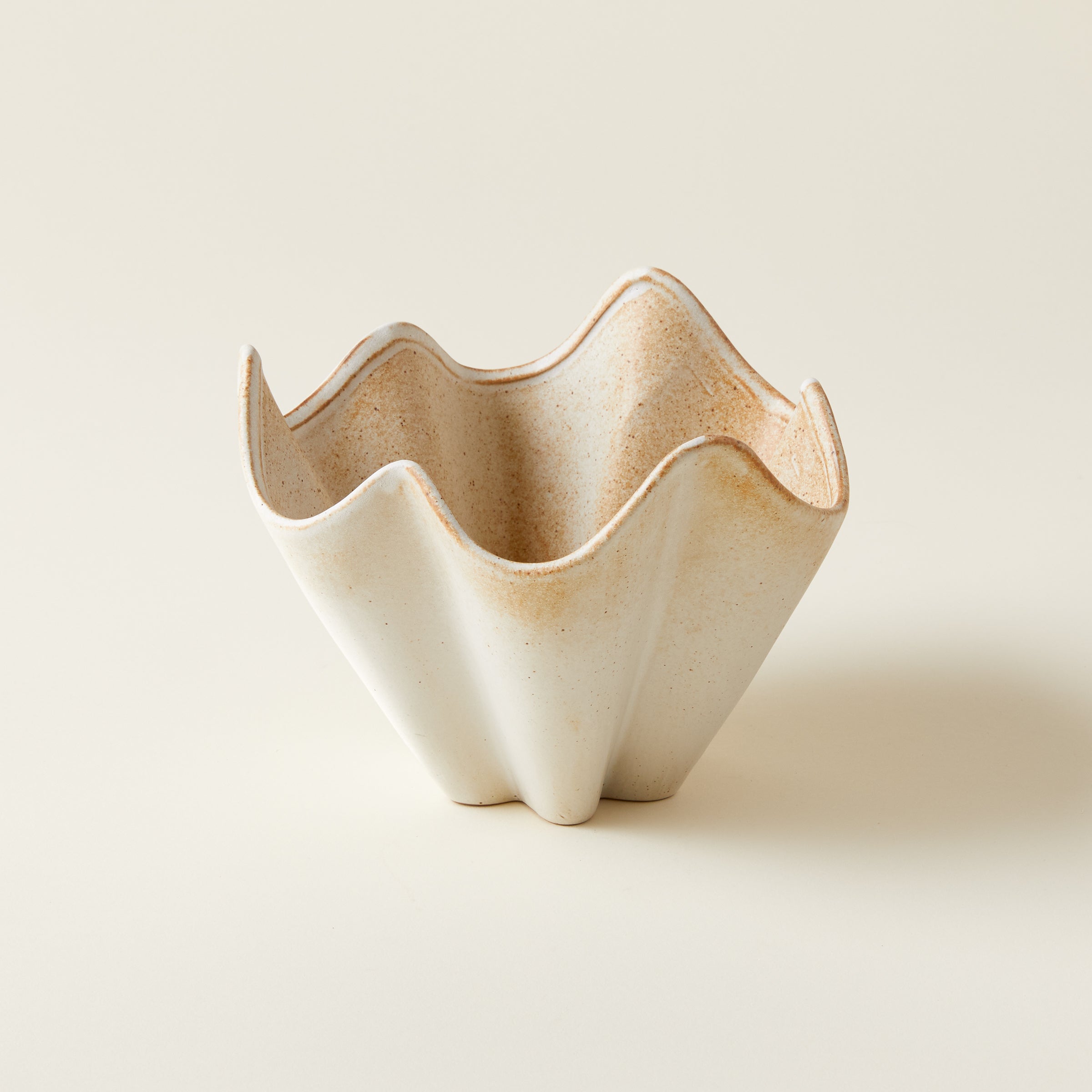A stoneware bowl with a pleated, wave-like design and a speckled cream-colored glaze.