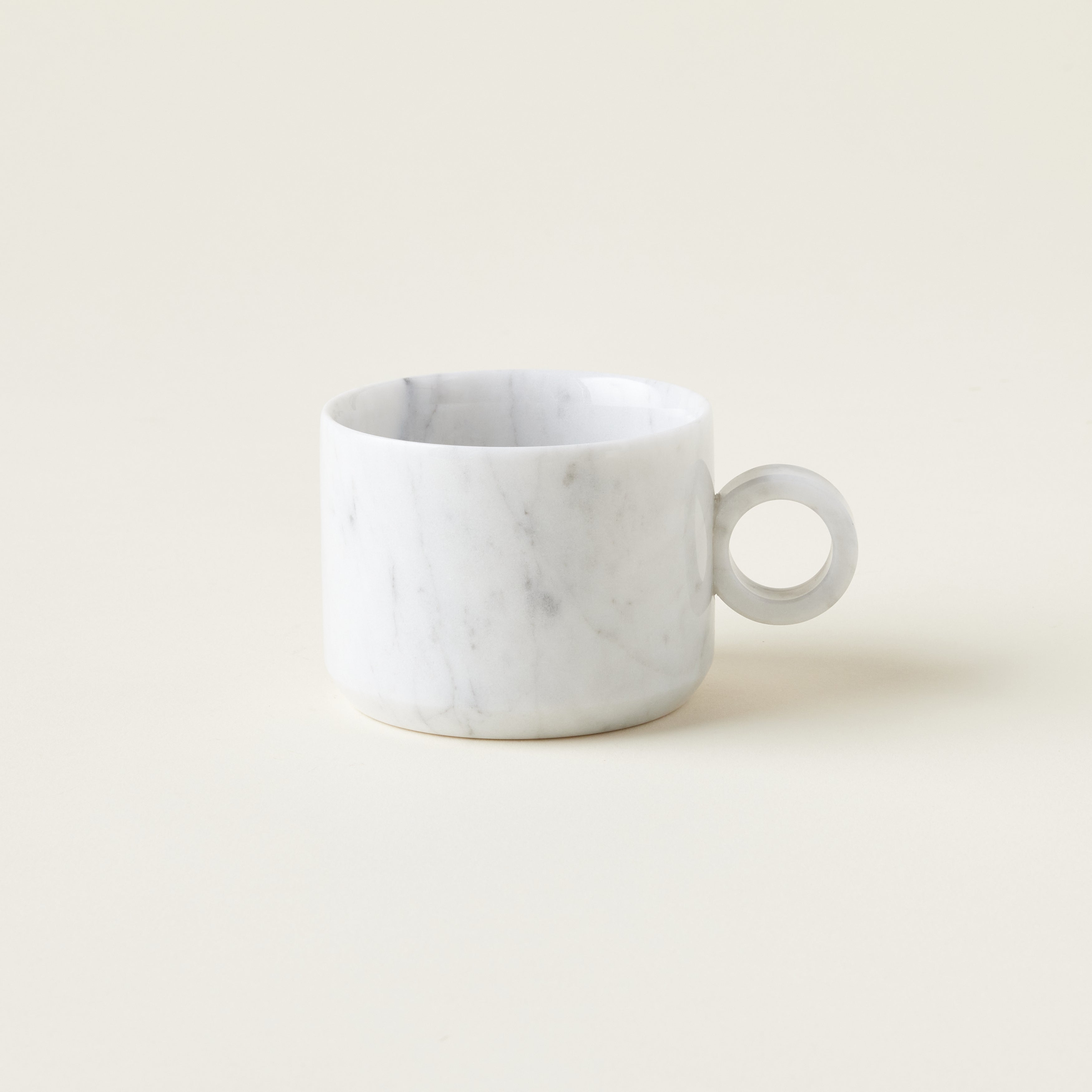 A smooth, white marble teacup with unique gray veining, shown from the side.