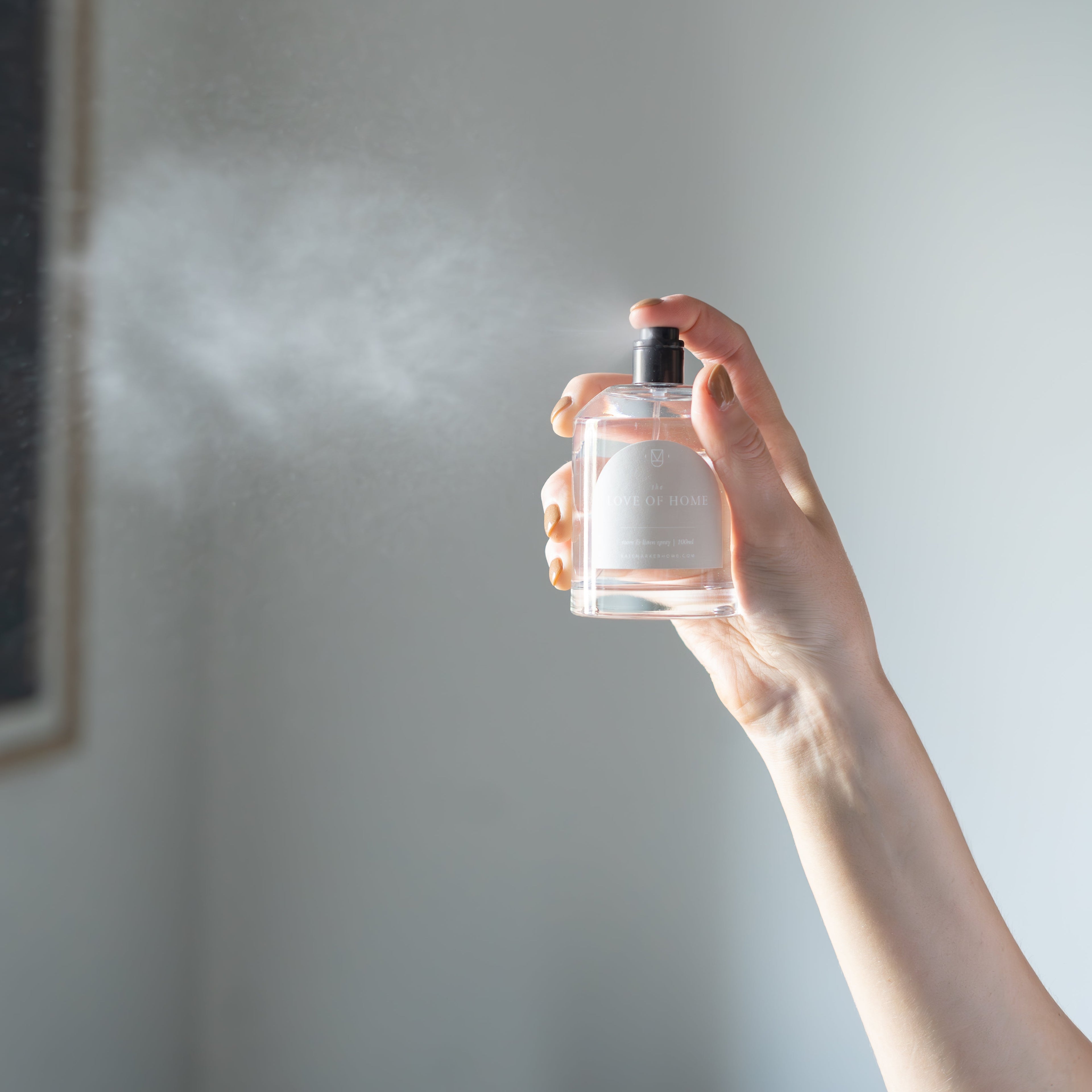 Hand holding a clear perfume bottle against a light gray wall