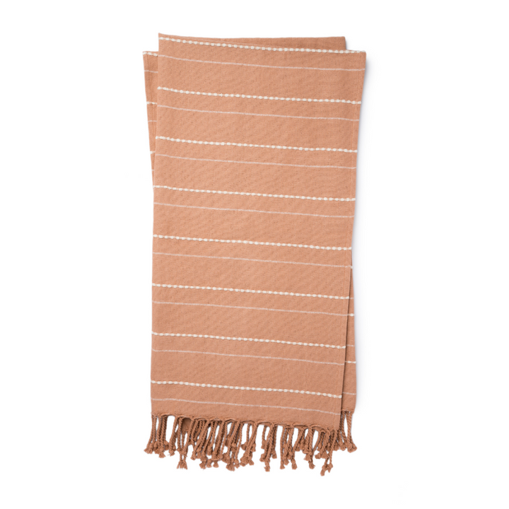 A cotton throw blanket in a deep blush color with decorative tassels.