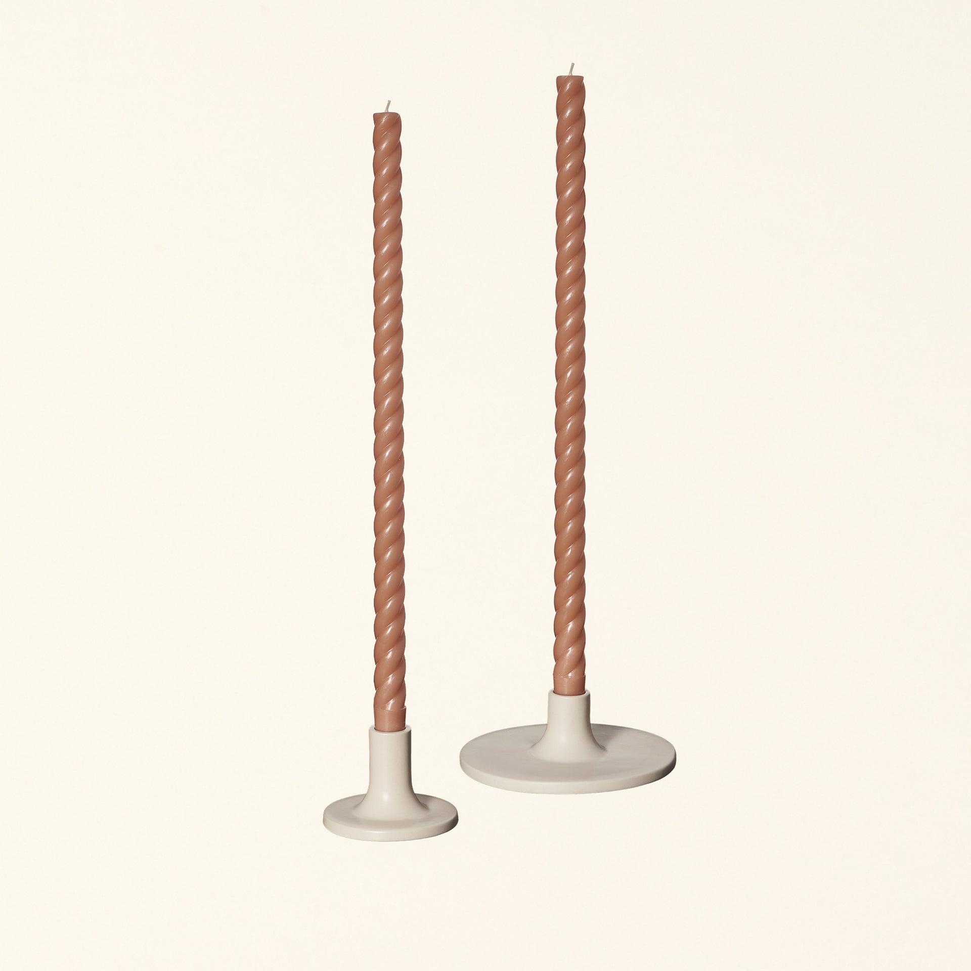 Set of two beige ceramic taper candle holders with candles.