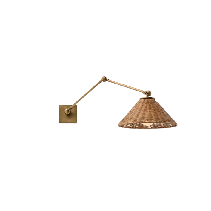 An articulating wall light with a woven wicker shade and an antique brass finish.