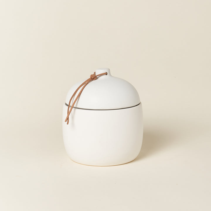 Ceramic jar with a lid and a leather strap.
