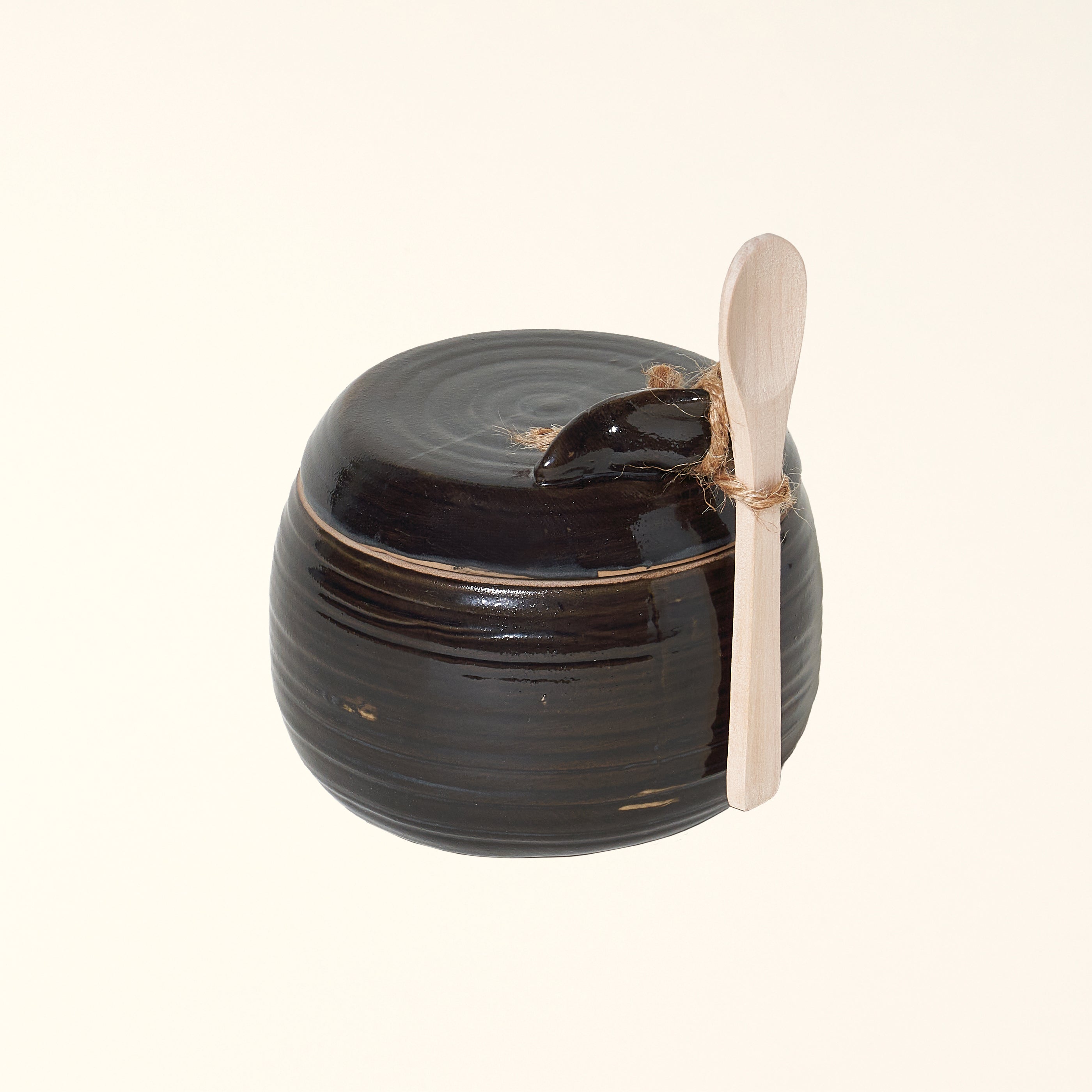Stoneware jar with a black reactive glaze finish and a wooden spoon.