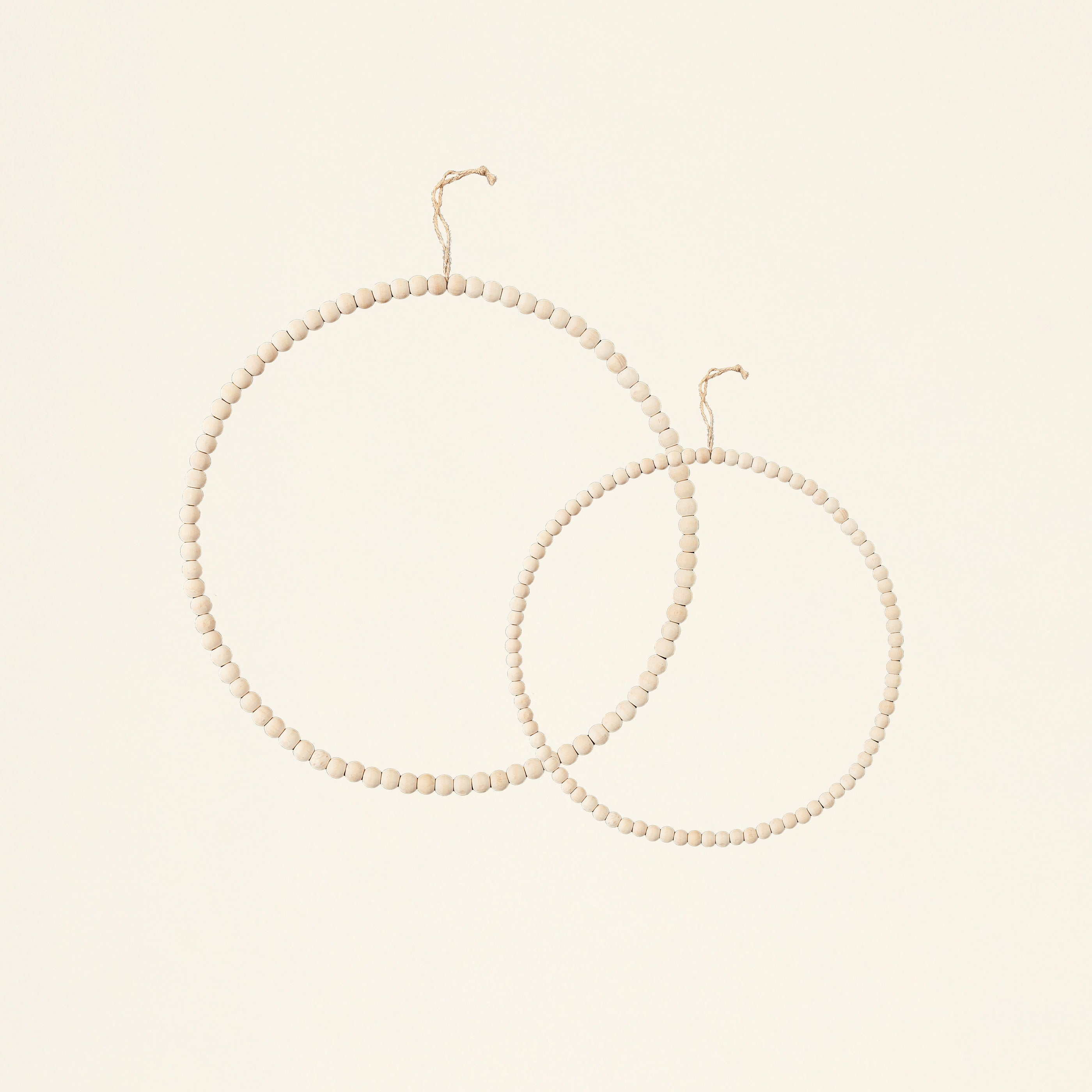 A set of two minimalist wreaths, one large and one small, made of white wooden and metal beads.