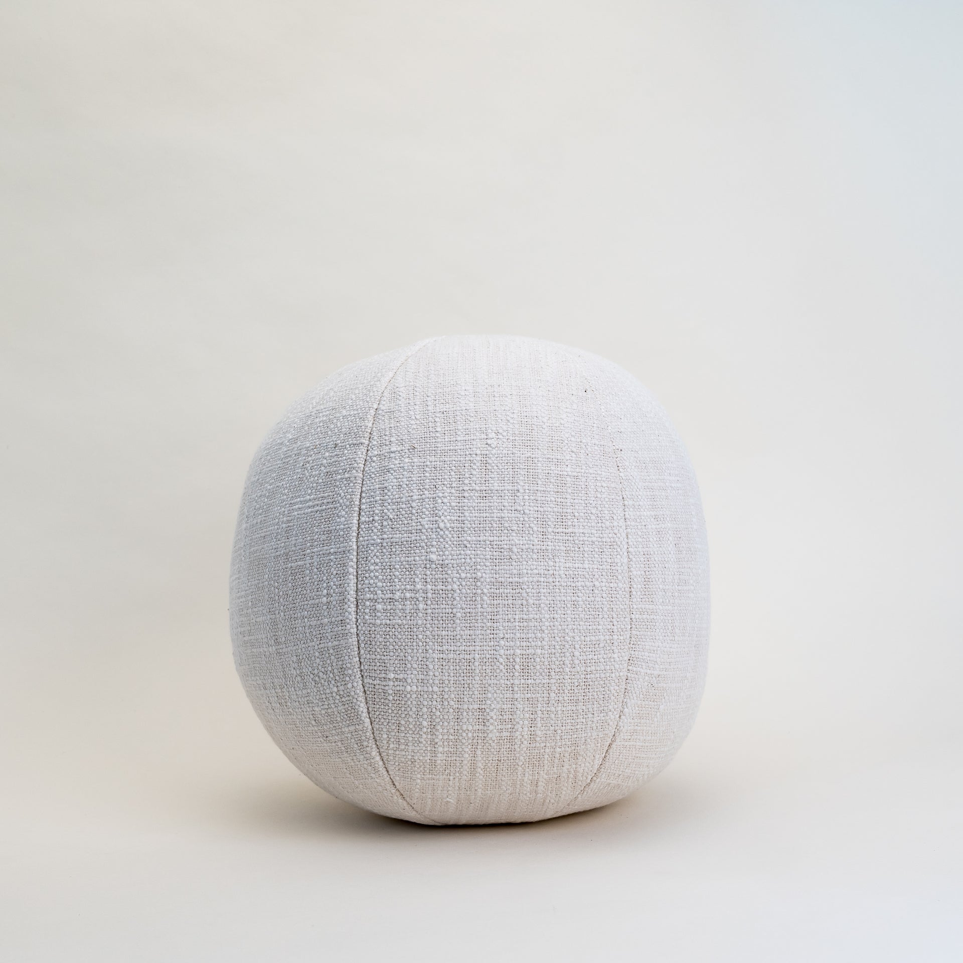 A round, cream-colored cotton orb pillow shown on a clean background, highlighting its unique shape and soft texture.