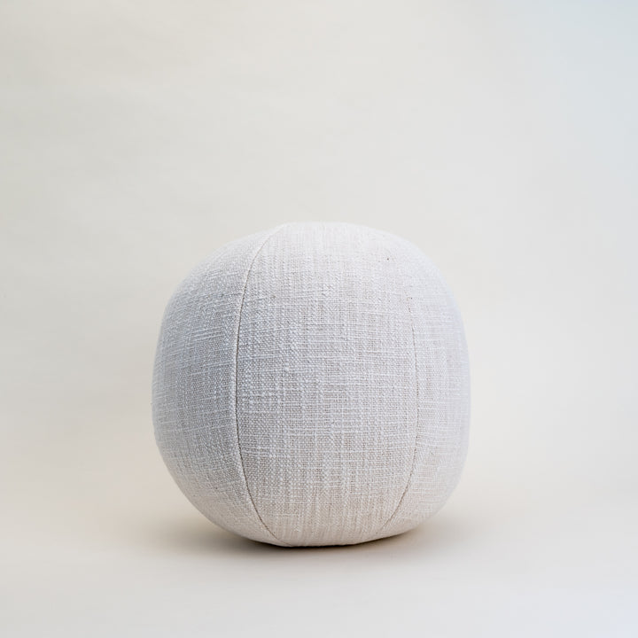 A round, cream-colored cotton orb pillow shown on a clean background, highlighting its unique shape and soft texture.