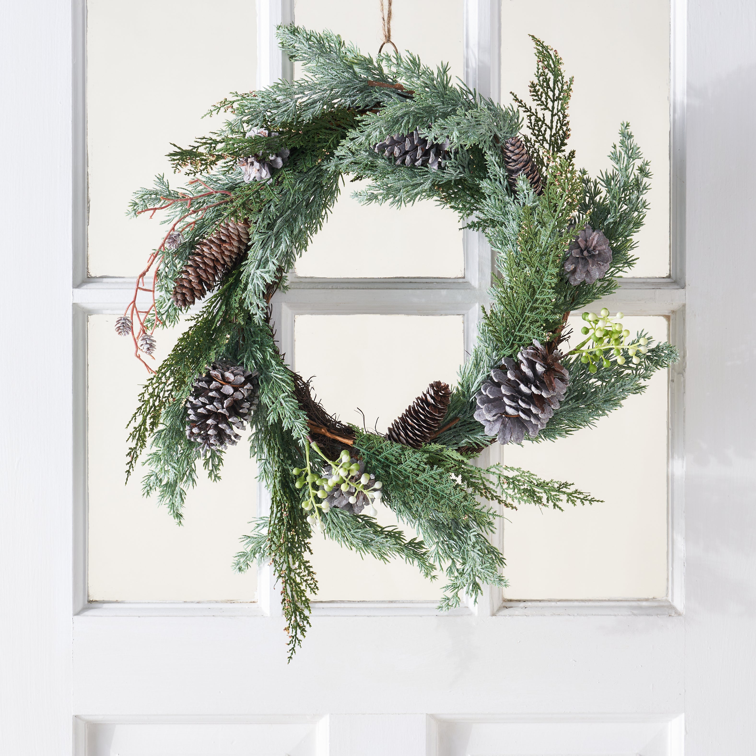 A decorative wreath with faux cedar sprigs and pinecones.