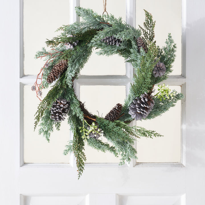 A decorative wreath with faux cedar sprigs and pinecones.
