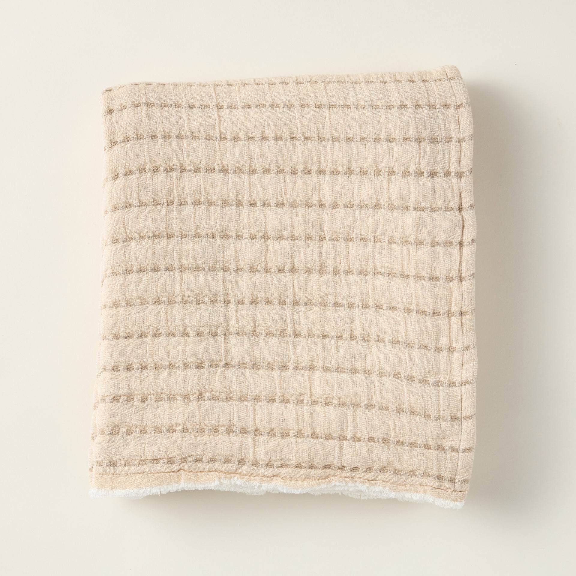 Two-tone double gauze cotton throw blanket on a sofa, with a neutral and brown side.