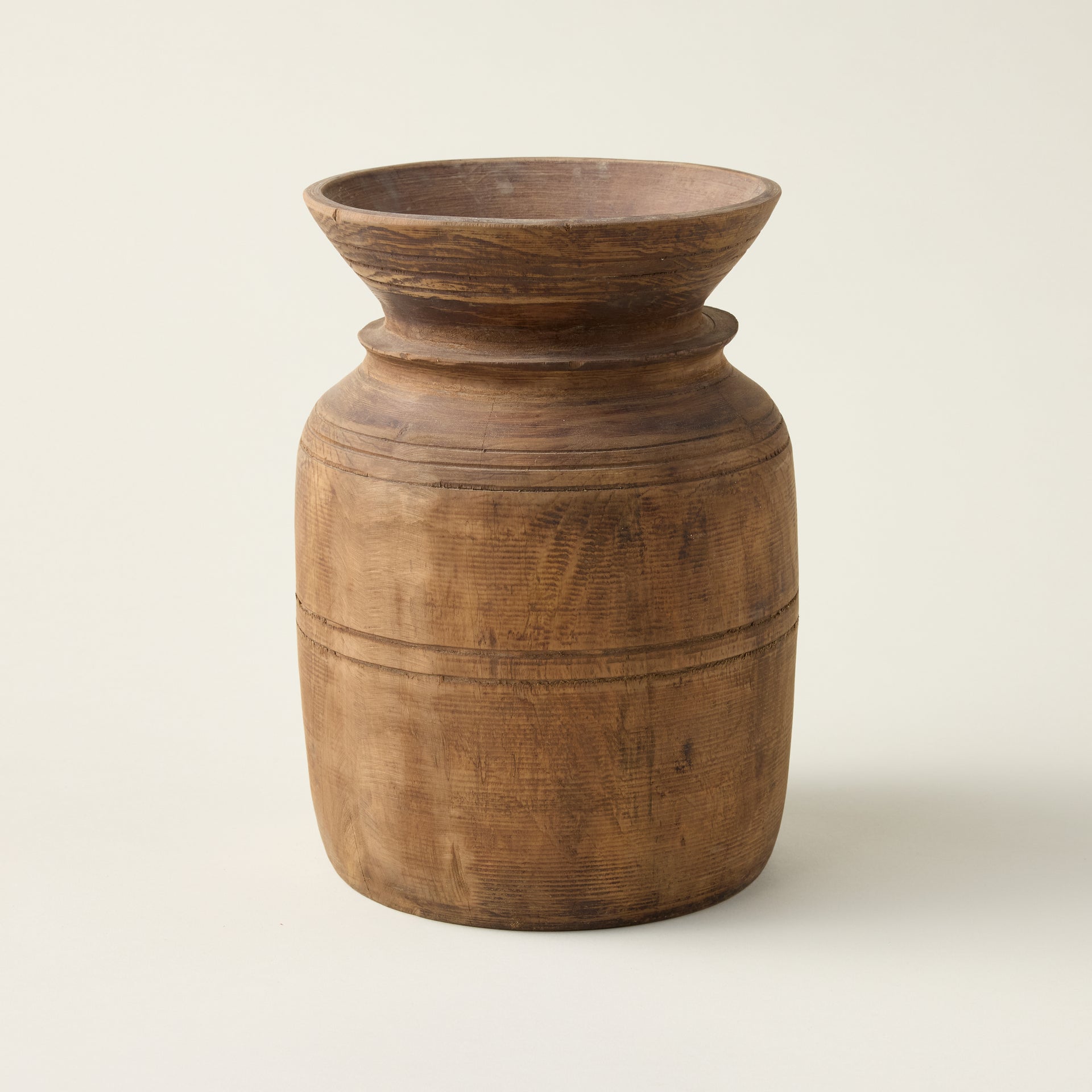 Artisanal Mango Wood urn with a sculptural design and natural finish, shown holding dried stems.