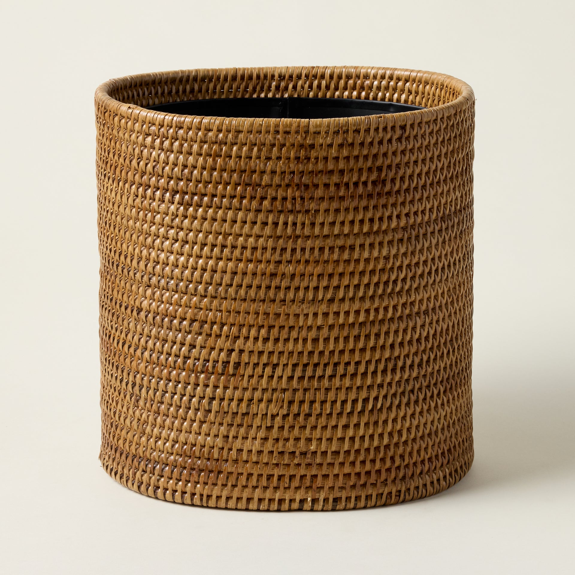 Hand-woven rattan oval wastebasket with a natural texture and an artisan-crafted design.