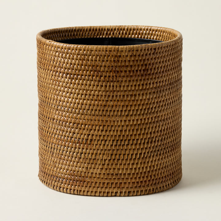 Hand-woven rattan oval wastebasket with a natural texture and an artisan-crafted design.