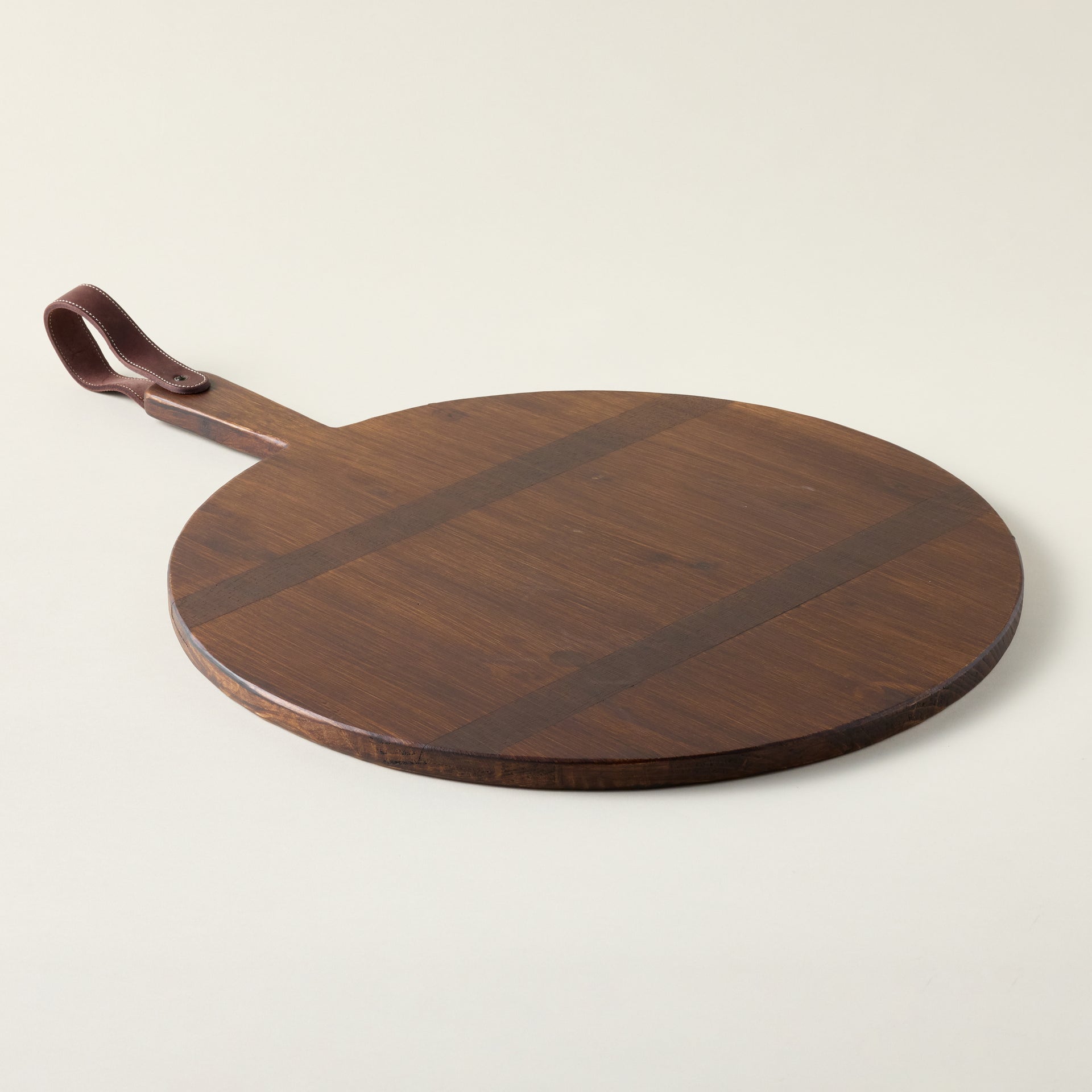Artisanal round charcuterie board crafted from reclaimed pine with a stitched leather strap.