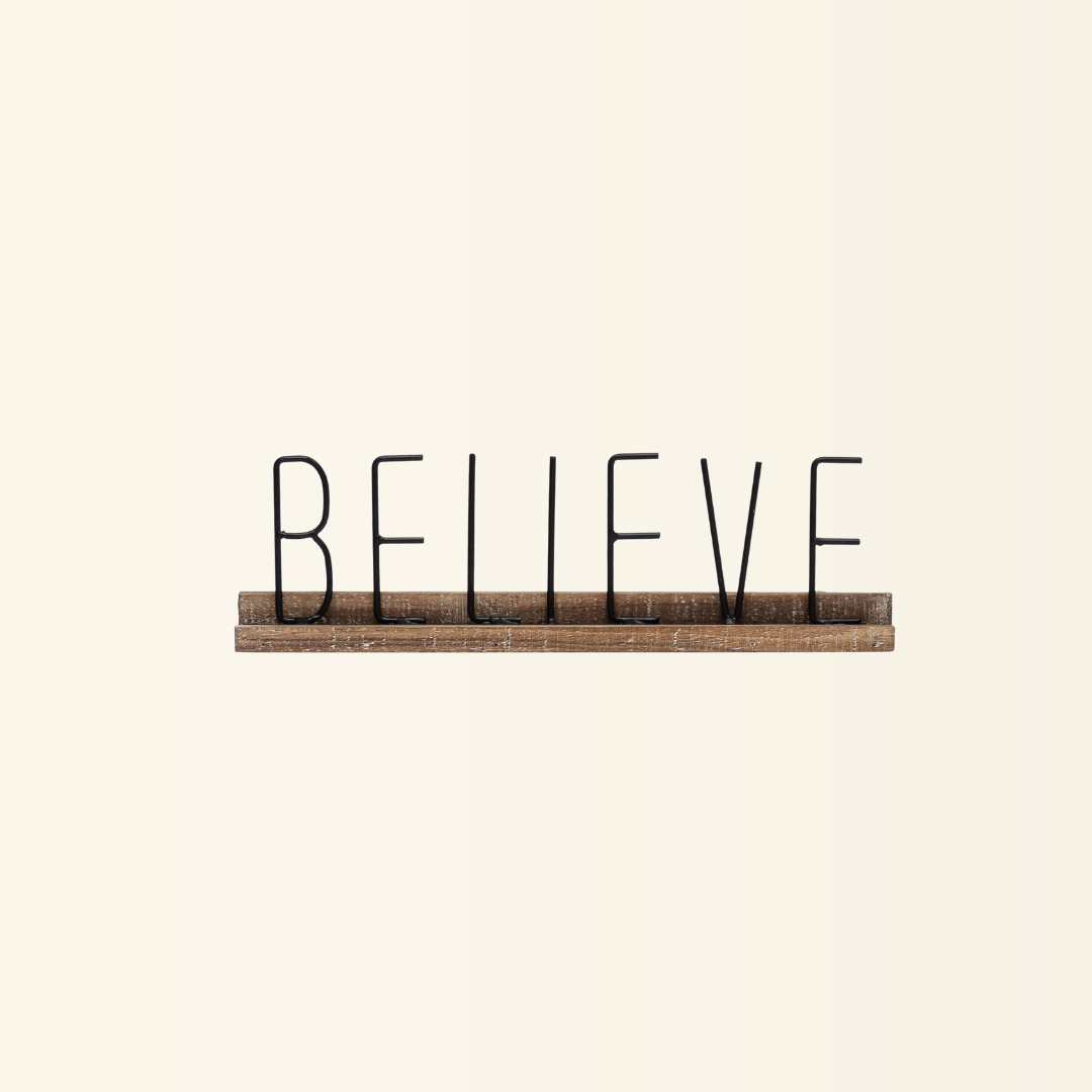 A decorative sign with the word "Believe" on a metal plate with a wooden base.